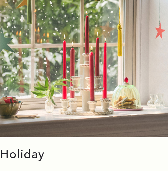 Red and white candles in holders on windowsill with snowy Christmas tree visible through window and holiday decorations