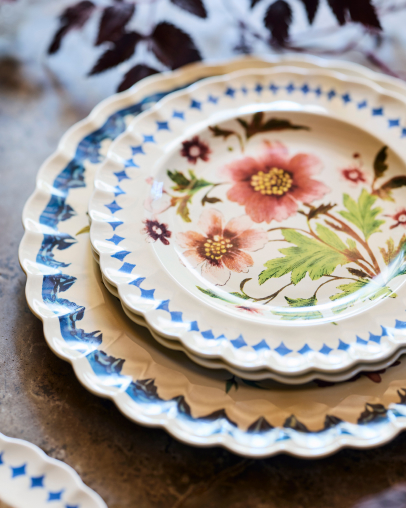 Stack of decorative paper plates with scalloped edges featuring floral patterns in pink, blue, and cream colors on a neutral surface.