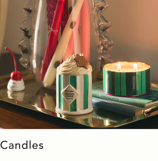 Two striped candles on a gold tray with books, one lit and one topped with whipped cream and a cherry decoration