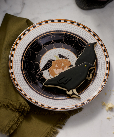 Halloween decorative plate with black cat silhouette, ravens, orange moon, and spider web design on white checkered border with orange and black trim.