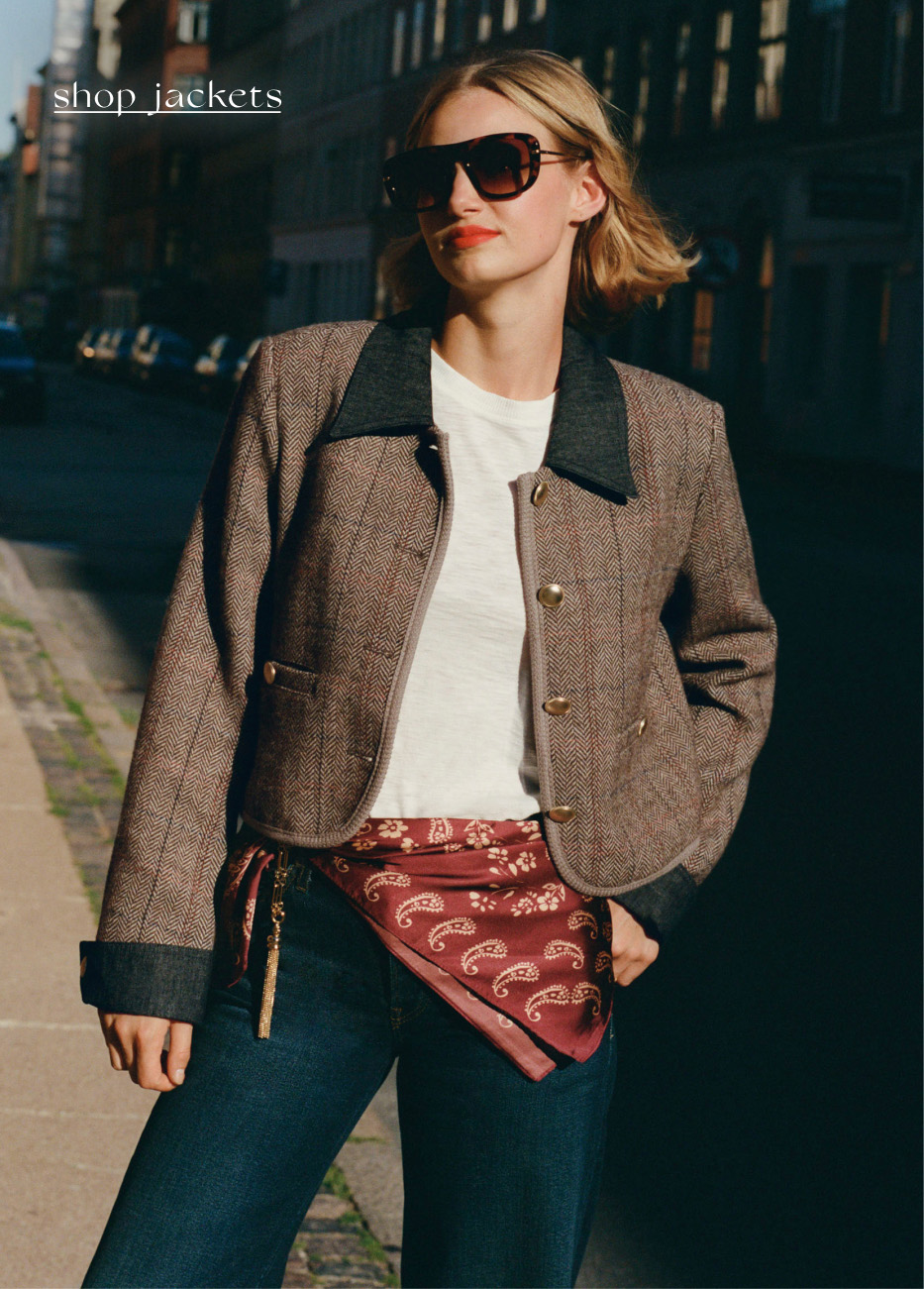 Woman in brown herringbone jacket with dark collar, white top, sunglasses, and red paisley clutch. Text reads shop_jackets.