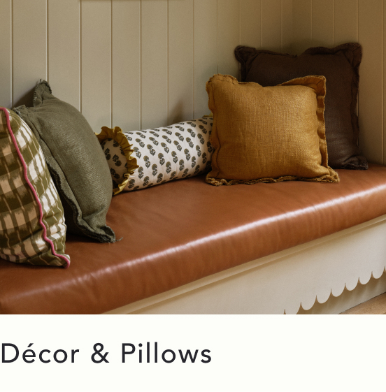 Decorative pillows in green plaid, white with black dots, mustard yellow, and brown arranged on a tan leather bench.