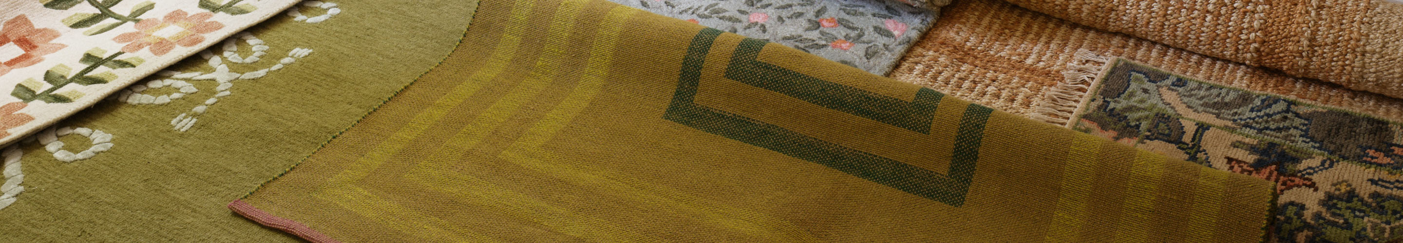 Layered decorative rugs in olive green, beige, and floral patterns with various textures and geometric designs.