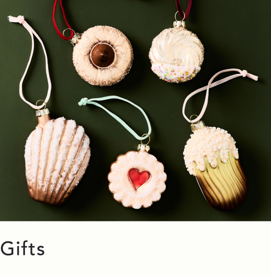 Five cookie-shaped ornaments with white ribbons on green background, including designs with chocolate, frosting, heart, and sprinkles