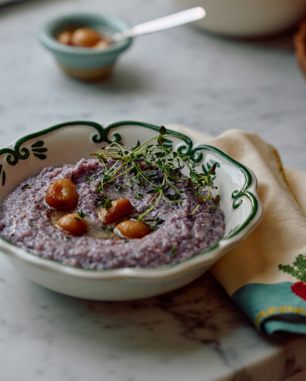 Purple hummus topped with chickpeas and fresh herbs in a decorative white bowl with green vine pattern on marble surface