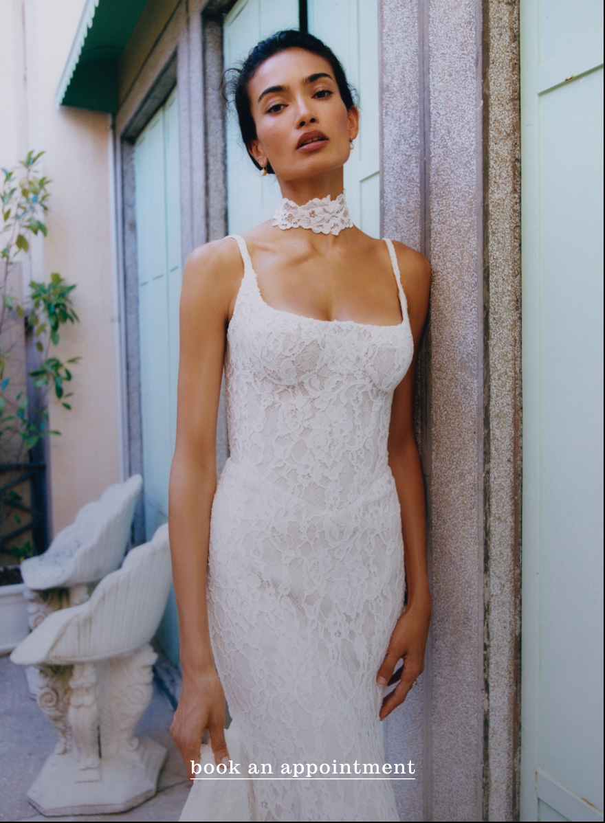 Woman in white lace dress with matching choker standing against stone column. Text reads book an appointment.