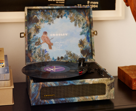 Vintage turntable playing a vinyl record with floral album cover featuring a bird and sunflowers on a dark surface.