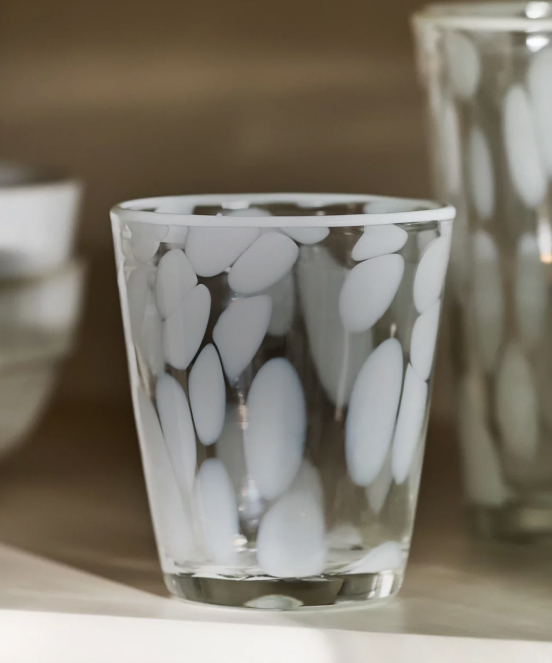 Clear glass with white oval pattern design on a neutral surface with blurred background objects.