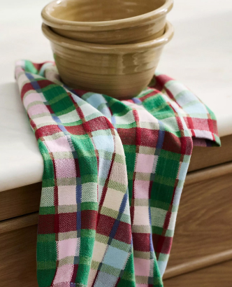 Two stacked beige ceramic bowls on a red, green, and white plaid kitchen towel draped over a wooden surface.