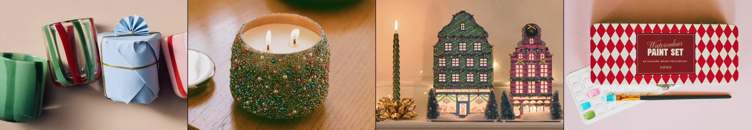Four holiday items: wrapped gifts with striped ribbon, glittery green candle, illuminated ceramic village houses, and watercolor paint set box.