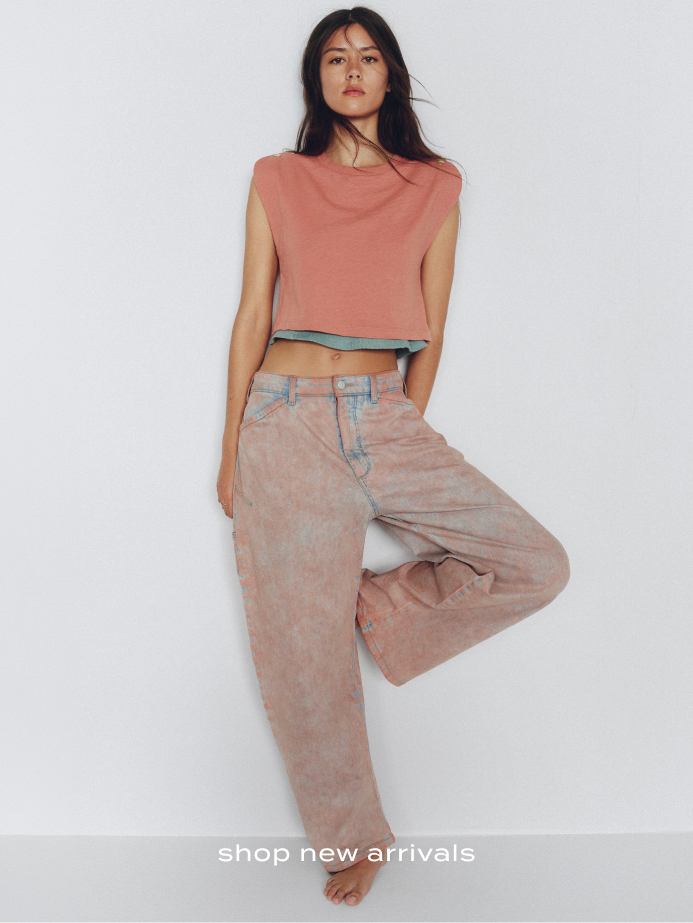 Woman wearing coral sleeveless crop top and beige wide-leg pants against white background with text shop new arrivals