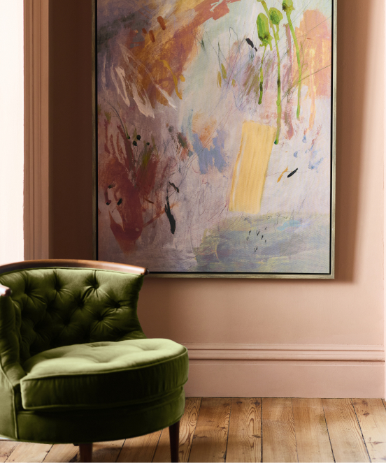 Abstract painting with orange, green, yellow, and blue brushstrokes hangs above a green velvet tufted chair on hardwood floor.