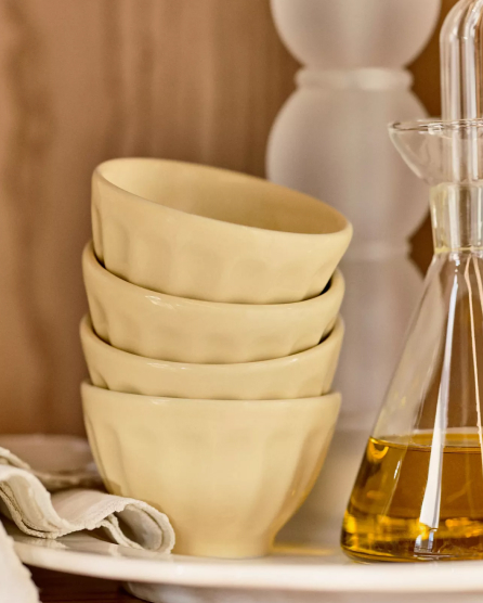 Stack of four cream-colored ceramic bowls next to a glass bottle of olive oil on a neutral-toned kitchen counter.