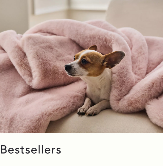 Small brown and white dog nestled in a plush pink blanket on a beige surface with text "Bestsellers" below