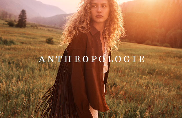 Black and white photo of woman with curly hair in white blouse sitting outdoors with ANTHROPOLOGIE text overlay