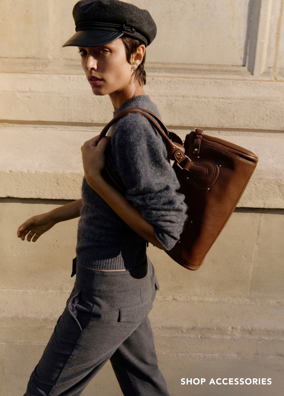 Woman wearing black newsboy cap and gray sweater carrying brown leather tote bag with text "SHOP ACCESSORIES"