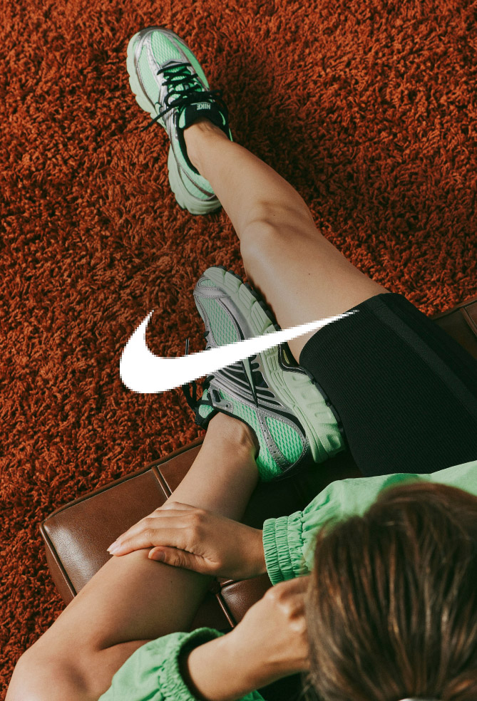Overhead view of person wearing green Nike running shoes with white swoosh logo on orange textured surface.