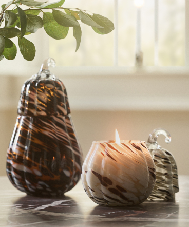 Two decorative glass objects with brown swirl patterns on a table, with green plant leaves above and a bright window behind.