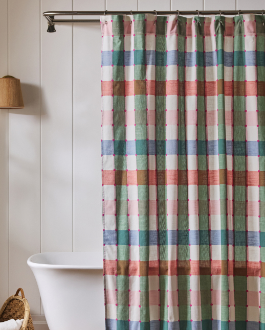 Plaid shower curtain in pink, green, and blue stripes hanging in white bathroom with freestanding tub and wicker basket.