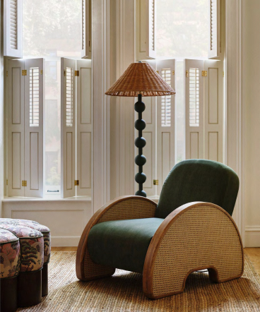 Green velvet armchair with woven rattan sides next to a tall floor lamp with black spherical base and wicker shade in a bright room.