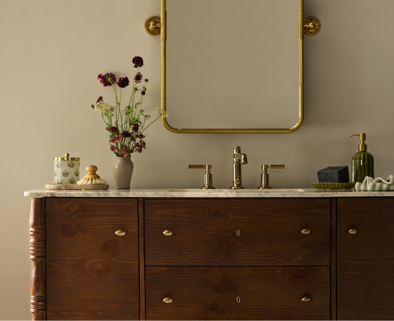 Elegant bathroom vanity with dark wood drawers, white marble top, brass faucet, gold-framed mirror, and purple flowers
