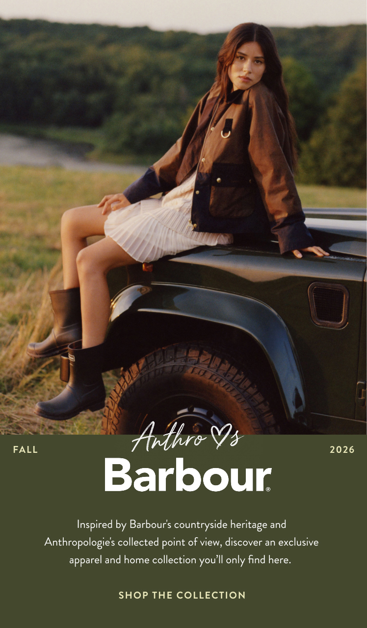 Woman in brown jacket and white skirt sitting on green vehicle in countryside. Text reads Anthro Loves Barbour Fall 2026.