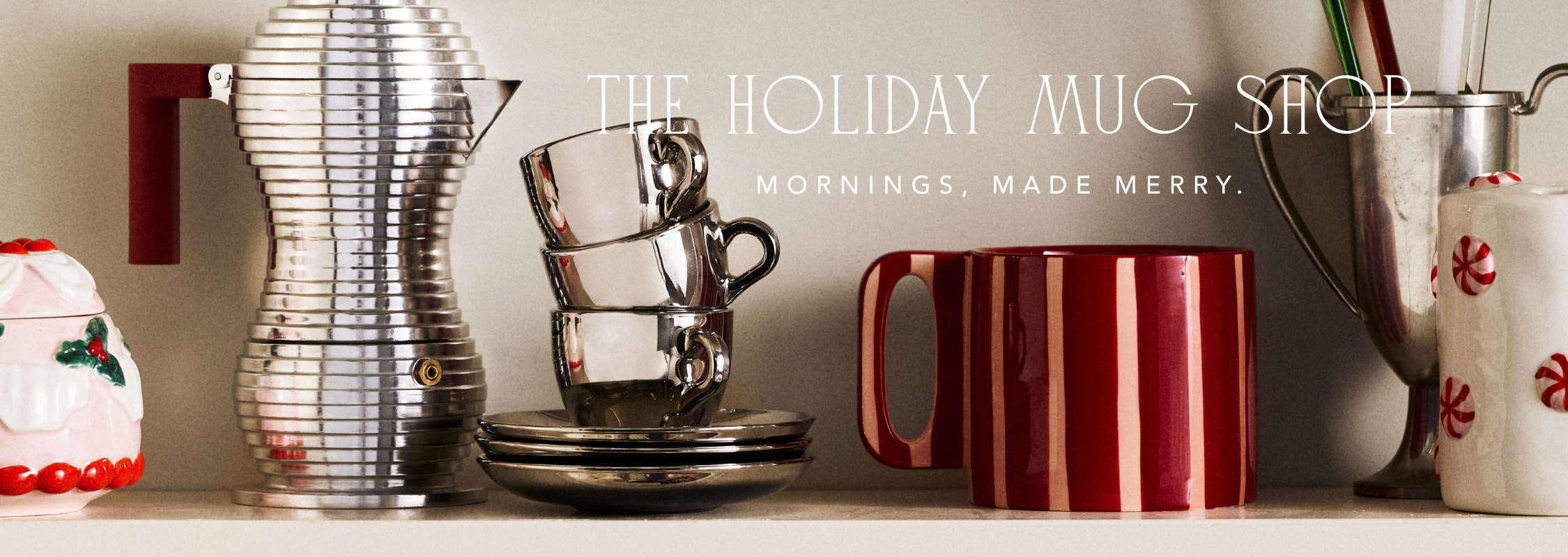 Holiday mugs and coffee accessories displayed on shelf with text "THE HOLIDAY MUG SHOP MORNINGS, MADE MERRY."