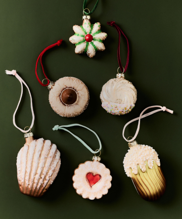Six festive ornaments shaped like cookies and treats on green background with white and red hanging ribbons.
