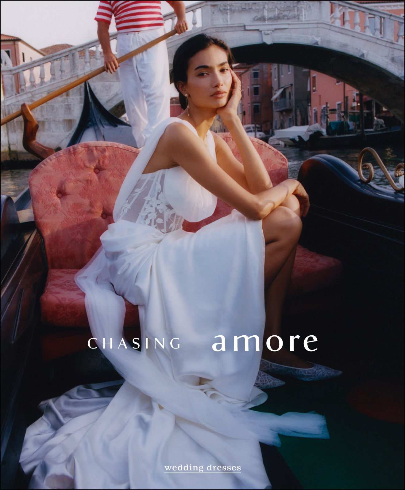 Woman in white wedding dress on gondola in Venice canal with gondolier and bridge. Text reads CHASING amore wedding dresses.