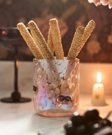 sesame seed breadsticks standing upright in a decorative glass jar with star patterns, candles glowing softly in the background.