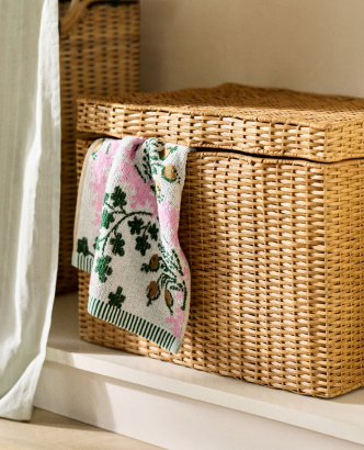 Woven wicker storage baskets on a white shelf with a folded floral towel draped over the front basket.