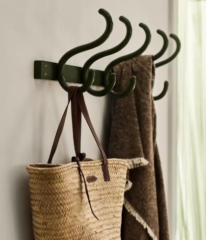 Wall-mounted coat rack with curved black hooks holding a woven straw tote bag with leather handles and a brown coat or scarf.