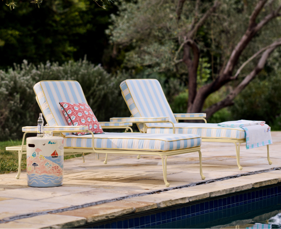 Two yellow and white striped lounge chairs beside a pool with a decorative cooler and red patterned towel in a garden setting.