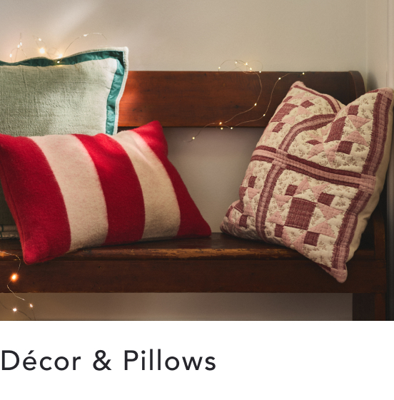 Decorative pillows on a wooden bench including red and white striped pillow and patterned cushions with fairy lights