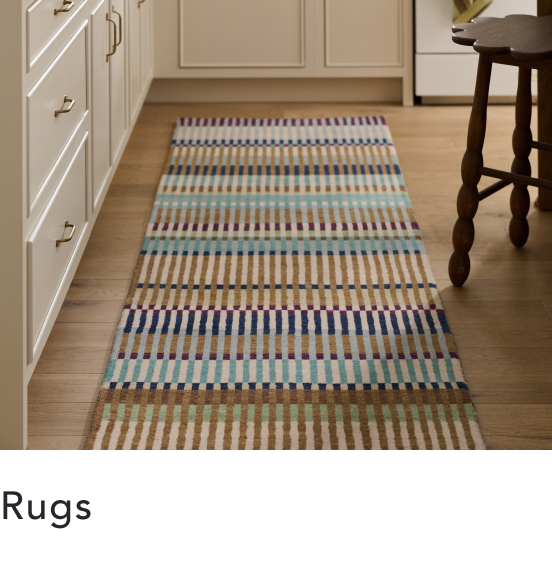 Colorful striped runner rug on hardwood floor in kitchen with white cabinets and wooden stool. Text reads "Rugs"