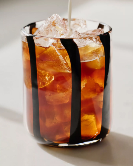 Iced tea in a black and white striped glass with ice cubes and a straw on a white surface.