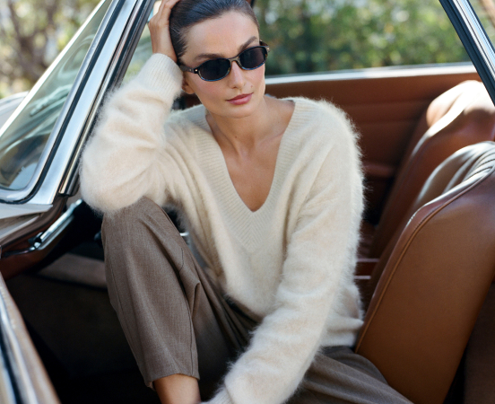 Woman wearing sunglasses and cream sweater sitting in vintage car with brown leather interior