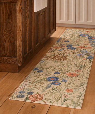 Floral patterned runner rug with blue and coral flowers on beige background, placed on hardwood floor beside dark wood cabinets.