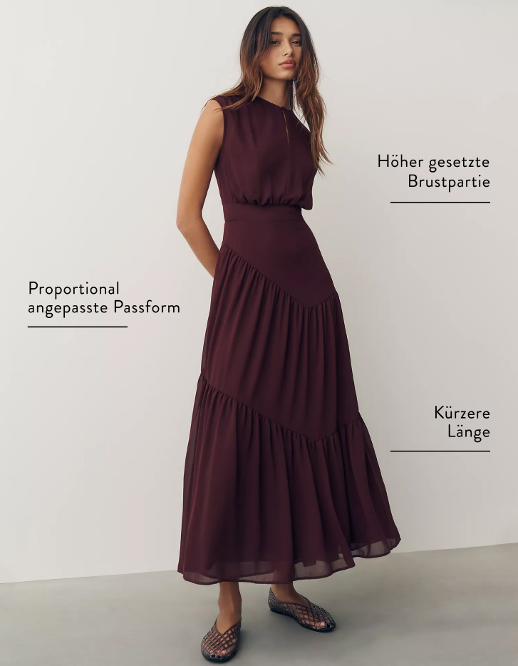 Woman in burgundy tiered maxi dress with labels indicating higher bust placement, proportionally scaled fit, and shorter length