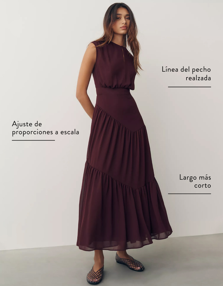 Woman in burgundy tiered maxi dress with labels indicating higher bust placement, proportionally scaled fit, and shorter length