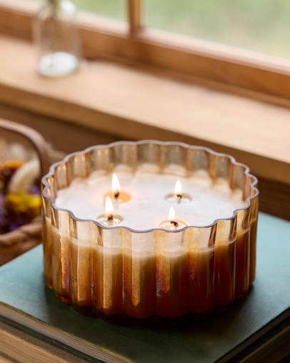 Gold ribbed multi-wick candle with white wax on green tray near window with flowers in background