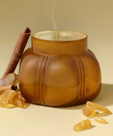Brown ceramic pot with steaming liquid, cinnamon stick, and amber crystals on beige surface against tan background.