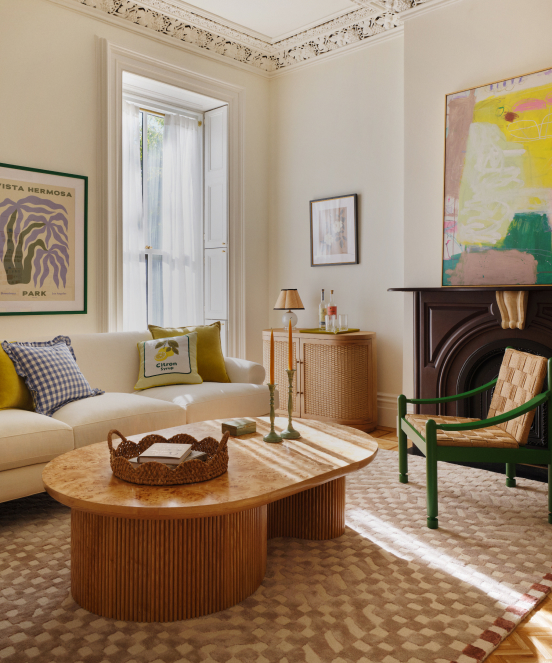 Bright living room with cream sofa, yellow and green accents, round wooden coffee table, fireplace, and decorative crown molding.