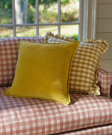 Yellow velvet pillow and gingham check pillows on a red and white checkered couch near a window with natural light