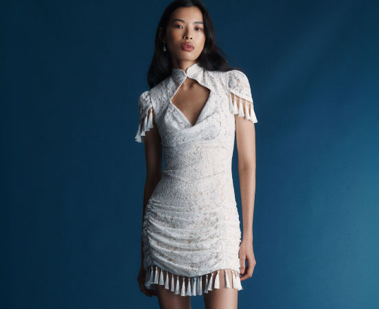 Woman in white sequined mini dress with fringe details and cutout neckline against blue background