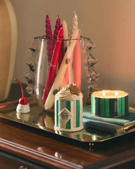 Decorative display with twisted pink and white candles in a silver holder, lit striped candle, and small dessert candle on tray.