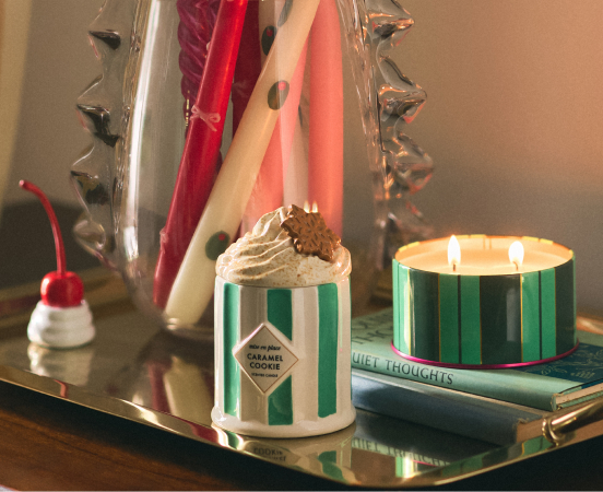 Two striped candles on a gold tray with books, one lit and one topped with whipped cream and a cherry decoration