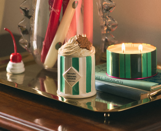 Green and white striped candle and caramel cookie dessert cup on gold tray with party decorations and balloons in background