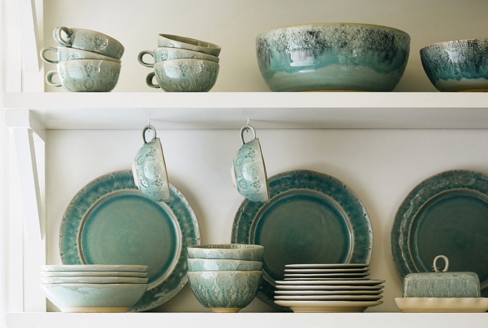 White shelves displaying turquoise and cream ceramic dinnerware including plates, bowls, cups, and serving dishes.