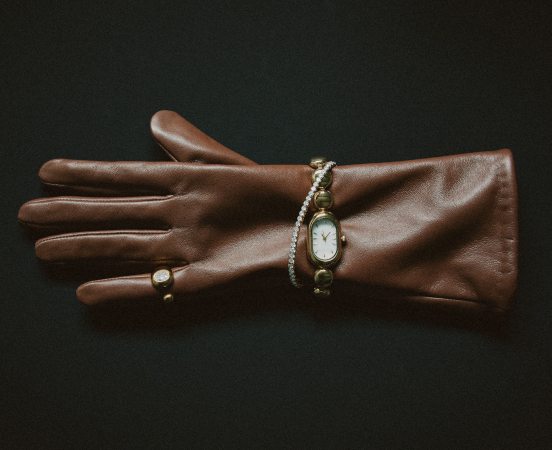 Brown leather glove with gold watch and ring on dark background